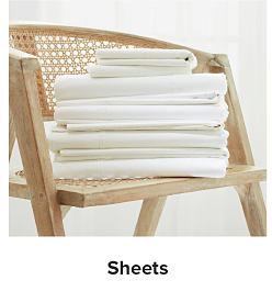 Stack of white linens on a woodene chair. Sheets. 