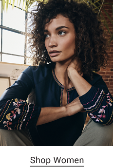 A woman wearing a navy blouse with floral embroidery on the sleeves. Shop women.