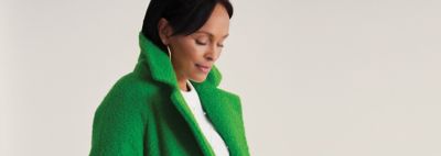 An image of a woman wearing a white top with a green coat.