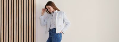 An image of a woman wearing a jacket over a white blouse with jeans.