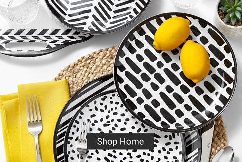 A dinnerware sit with different black and white patterns. Some are dotted, some are splotched, some have lines on them. Two lemons sit atop one of the plates, matching the yellow napkins. Shop home. 