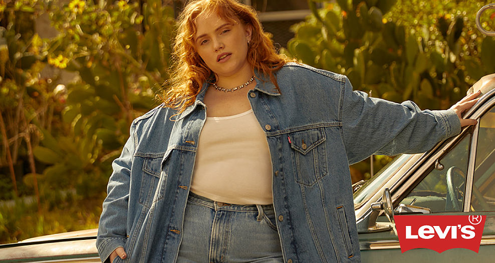 A woman in a denim jacket, white tank and blue jeans. She is leaning against a classic car. Levi's. 