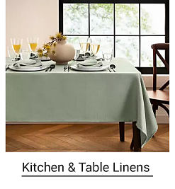 A table set with dinnerware and wine glasses, covered with a light green tablecloth. Shop kitchen and table linens.
