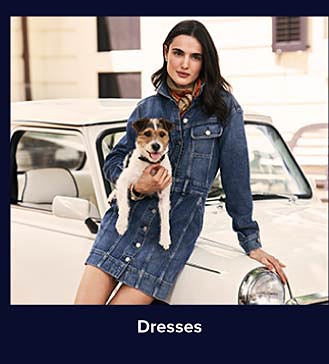 An image of a woman in a denim dress holding a dog. Shop dresses.