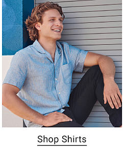 A man in a blue short sleeve button down shirt and black jeans. Shop shirts.