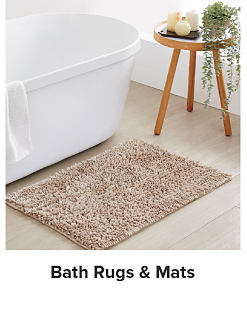 A bathtub with a table and a rug next to it. Shop bath rugs and mats.