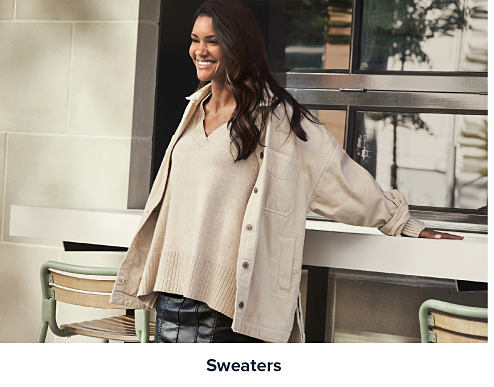 Image of a woman wearing a beige dress and jacket. Shop sweaters. 