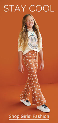 Stay cool. Image of a girl in orange pants and a long sleeve shirt with a smiley face on it. Shop girls' fashion.