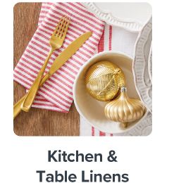 Red and white table linens and a bowl with gold ornaments inside. Shop kitchen and table linens.