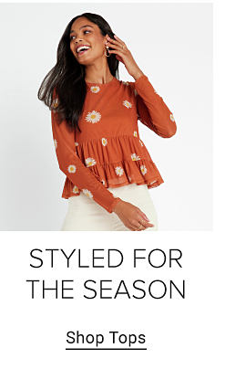 Young woman wearing a burnt orange blouse with white flower pattern. Styled for the season. Shop tops