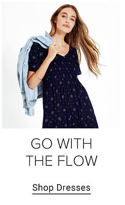 Young woman wearing a dark blue polka dot dress. Go with the flow. Shop dresses