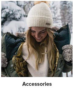 A woman wearing a white knit hat, a puffer jacket and gloves. Shop accessories.