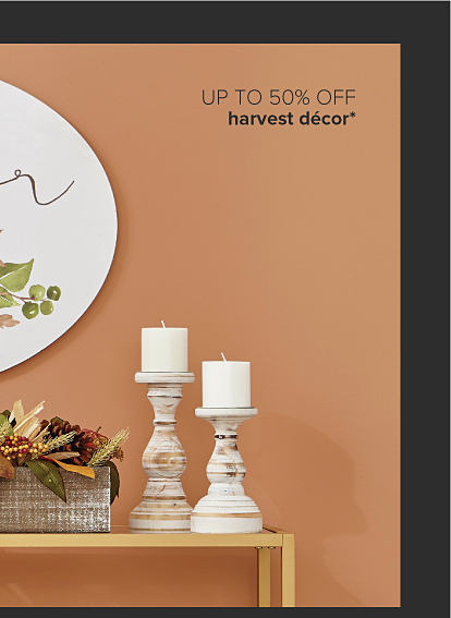 Orange wall with a piece of art that says gather and has pumpkins on it. Underneath there is a gold console table with a frame photo of a dog that says thankful, candles and a basket of fall foliage and pinecones. Up to 50% off harvest decor