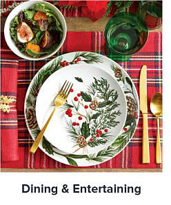 Image a plaid table setting with a white Christmas themed plate and gold flatware. Shop dining and entertaining.