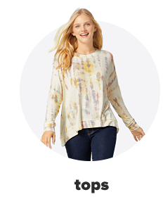 A young woman wears a yellow tie-dye top paired with dark blue jeans. Shop tops.