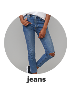 A woman wears distressed blue jeans with a rip in one knee. Shop jeans.