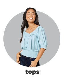 A young woman wears a light blue three quarter length blouse and jeans. Shop tops.