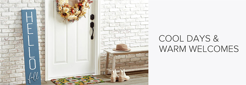 A front door surrounding by white brick. Fall decor includes an autumn wreath, a blue sign that says hello fall and a floral welcome mat. On a bench sits a hat, and in front of it sits a pair of boots. Cool days and warm welcomes. 