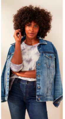 A woman in a light blue and white tie dye sweater with a denim jacket and dark denim jeans.