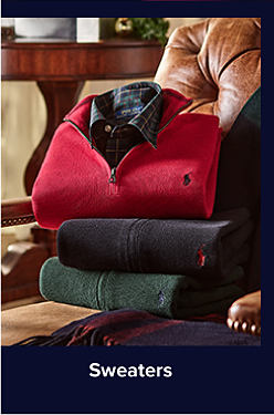 An image of quarter zip sweaters and a plaid button down shirt stacked on a chair. Shop Sweaters.