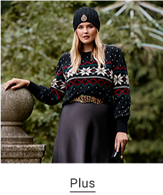 A woman wearing a green, red and white snowflake print sweater, a green winter hat and a black skirt. Plus.