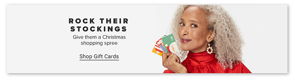 A woman in a red dress holding Belk gift cards. Rock their stockings. Give them a Christmas shopping spree. Shop gift cards. 