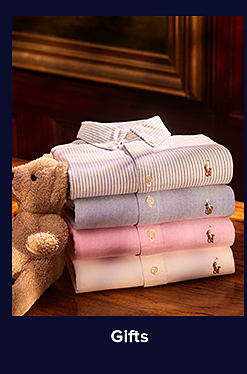 An image of a stuffed Polo Bear next to a stack of colorful button-down Polo shirts. Shop gifts.