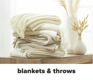 A stack of quilts and bed blankets in cream and white. Shop blankets and throws. 