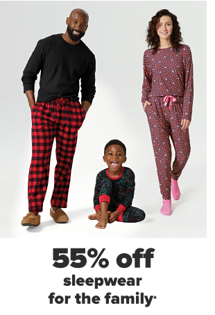 A man in a black long sleeve shirt and red plaid pajama pants. A little boy in a red, black and green pajama set. A woman in a red and pink patterned pajama set. 55% off sleepwear for the family. 