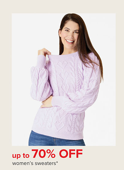 A woman in a pink sweater with a textured heart pattern. Up to 70% off women's sweaters.