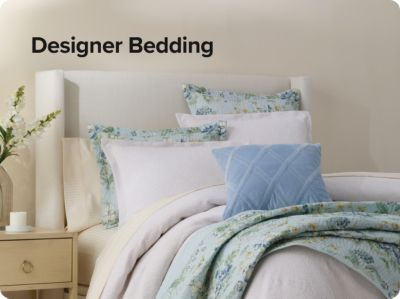 Shop designer bedding. A bed with floral decorative pillows and blankets. 